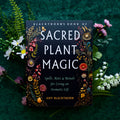 Book titled 'Blackthorn's Book of Sacred Plant Magic' surrounded by flowers on a dark green background