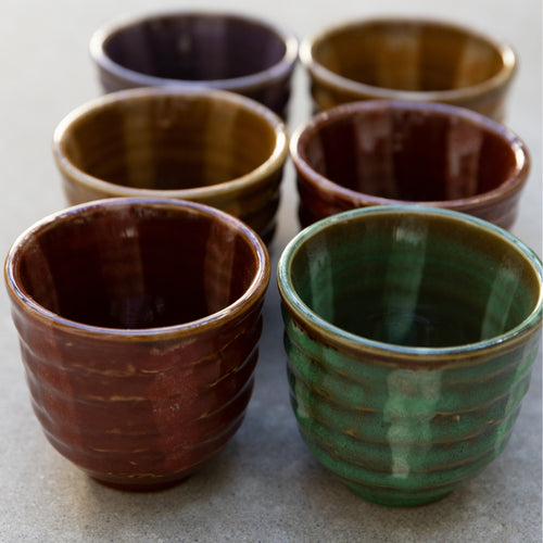 Set of six ceramic cups in various colors on a light surface