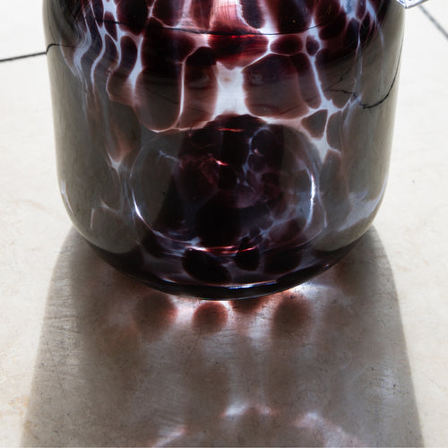 Glass container with purple and white marbled pattern on a light surface