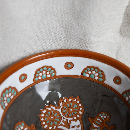 Decorative ceramic plate with brown and turquoise patterns on a neutral background