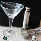 Clear martini glass with cocktail shaker and jigger on a dark background