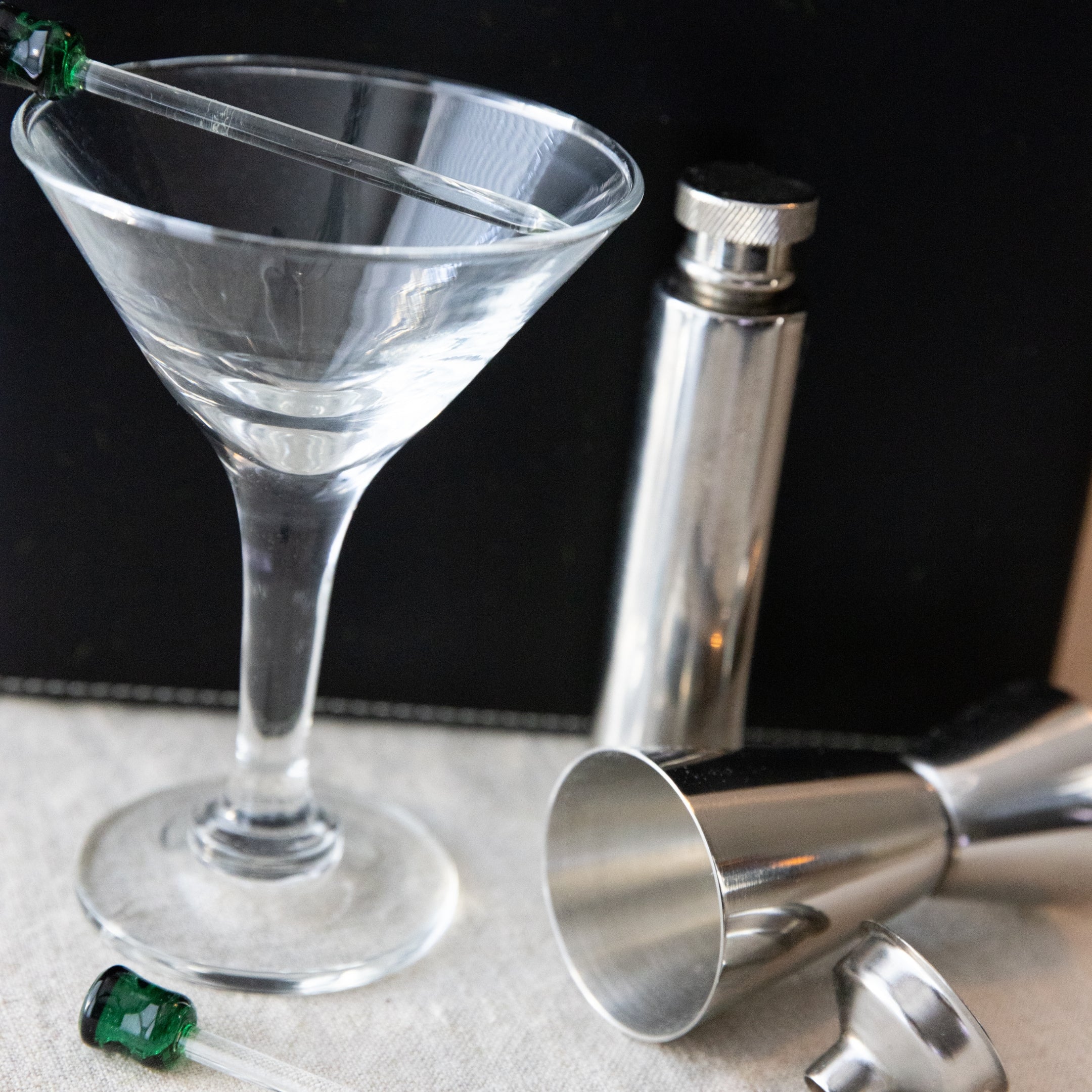 Clear martini glass with cocktail shaker and jigger on a dark background
