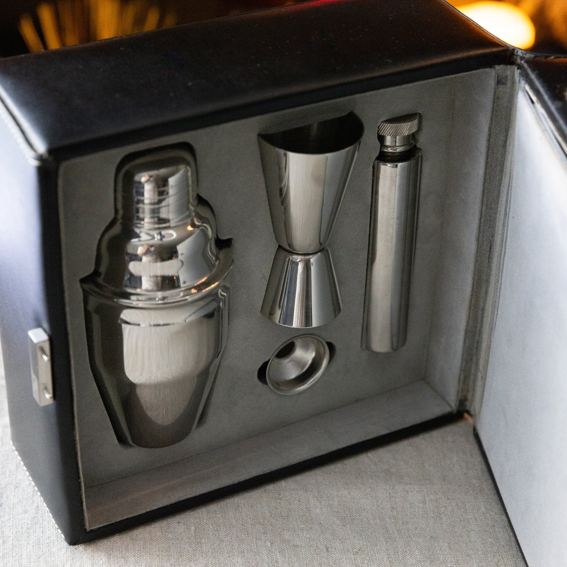 Set of cocktail-making tools including a shaker, jigger, and flask in a black box.