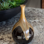 Decorative vase with black and gold gradient on a marble surface with a plant in the background