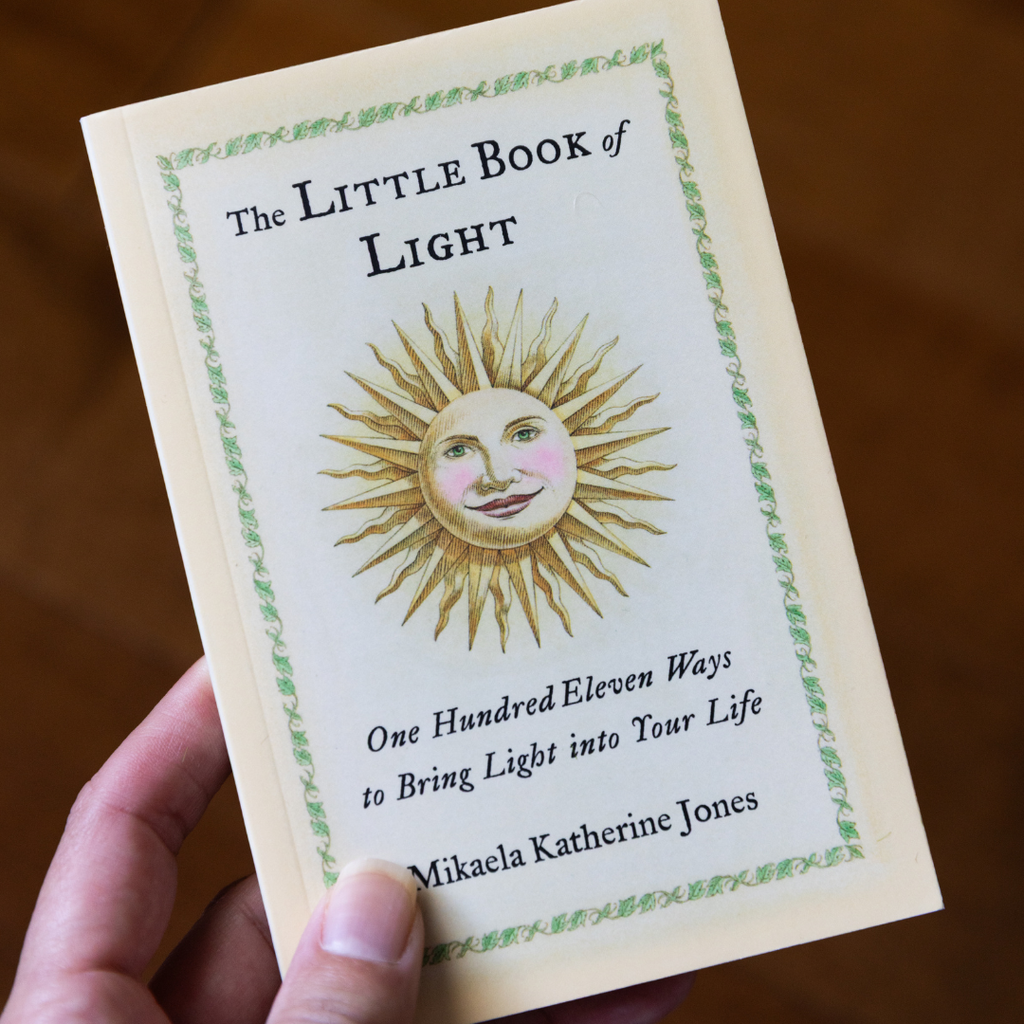 Book titled 'The Little Book of Light' held by a hand on a wooden surface