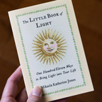 Book titled 'The Little Book of Light' held by a hand on a wooden surface
