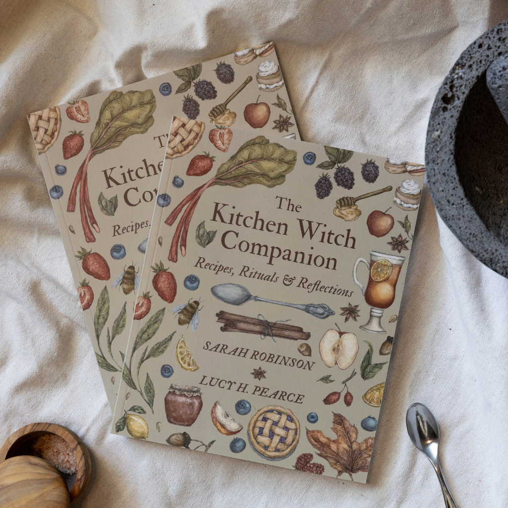 Two books titled 'The Kitchen Witch Companion' on a white fabric background.