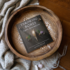 Book titled 'Throwing Bones' on a wooden tray with a textured surface and soft lighting.