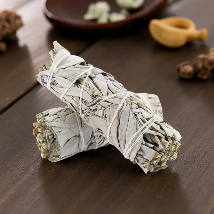 Two bundles of sage tied together on a wooden surface with blurred background