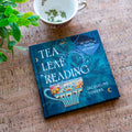 Book titled 'Tea Leaf Reading' by Jacqueline Towers on a textured surface with a cup and plant.