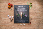 Book titled 'Throwing Bones' with crystals and stones on a cork background
