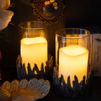 Two lit candles in decorative holders on a dark surface with a decorative plate and books in the background.